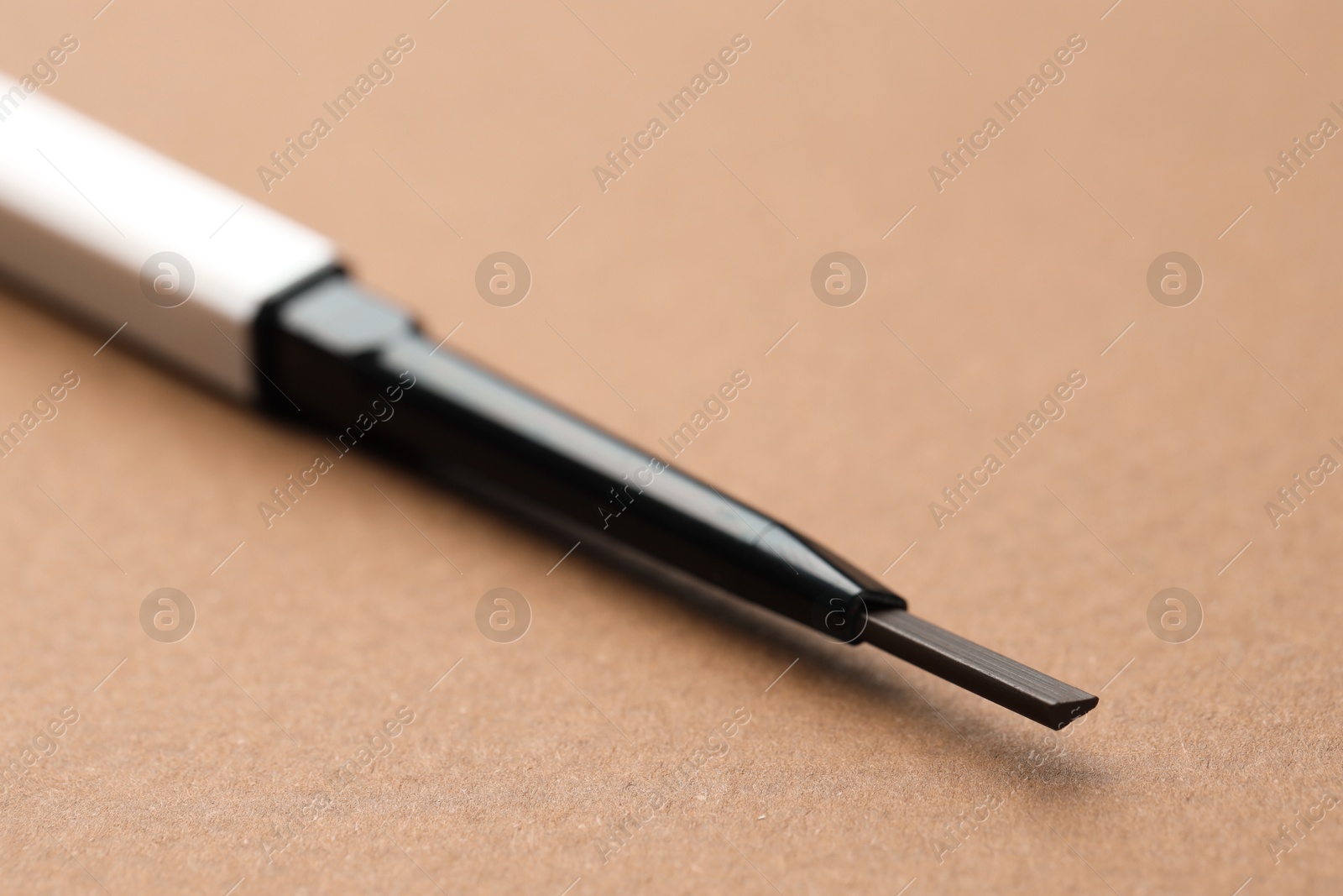 One automatic eyebrow pencil on brown background, macro view Photo of One automatic eyebrow pencil on brown background, macro view