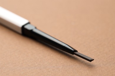 Photo of One automatic eyebrow pencil on brown background, macro view