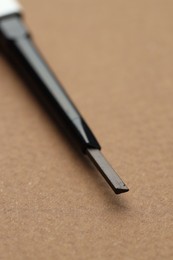 Photo of One automatic eyebrow pencil on brown background, macro view