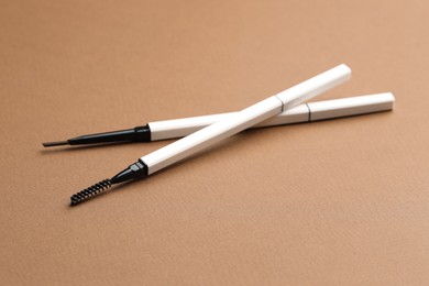Photo of Automatic eyebrow pencils on brown background, closeup