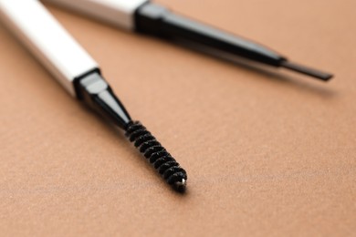 Photo of Automatic eyebrow pencils on brown background, macro view