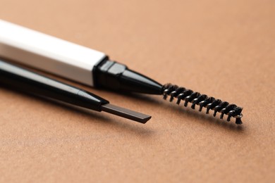 Photo of Automatic eyebrow pencils on brown background, macro view