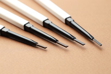 Photo of Automatic eyebrow pencils on brown background, macro view
