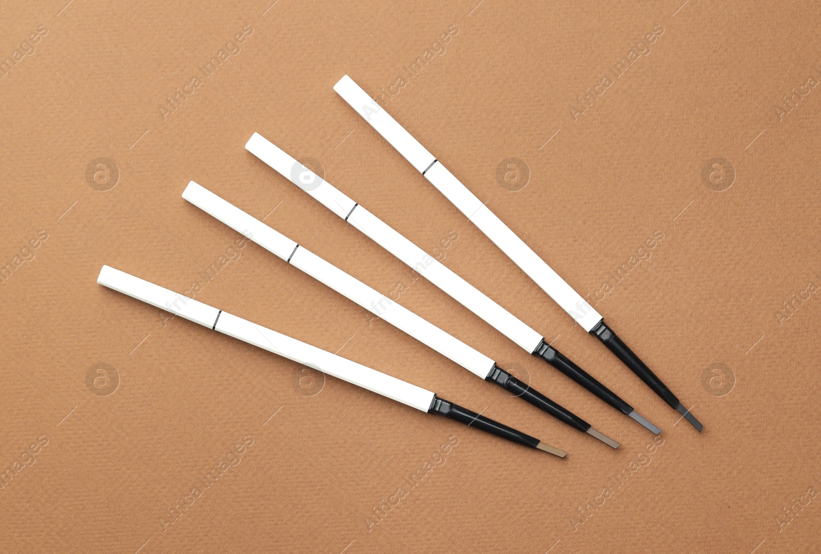 Different eyebrow pencils on brown background, flat lay Photo of Different eyebrow pencils on brown background, flat lay