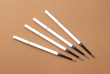 Photo of Different eyebrow pencils on brown background, flat lay