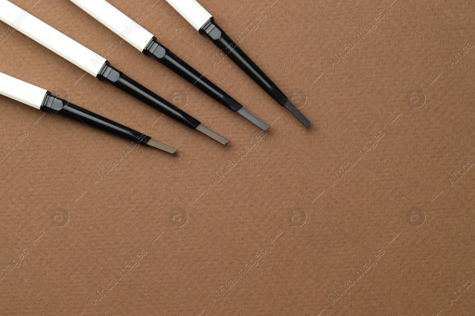 Different eyebrow pencils on brown background, flat lay. Space for text Photo of Different eyebrow pencils on brown background, flat lay. Space for text