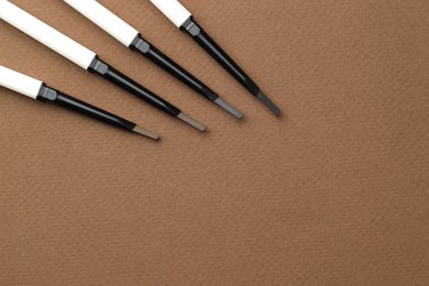 Photo of Different eyebrow pencils on brown background, flat lay. Space for text