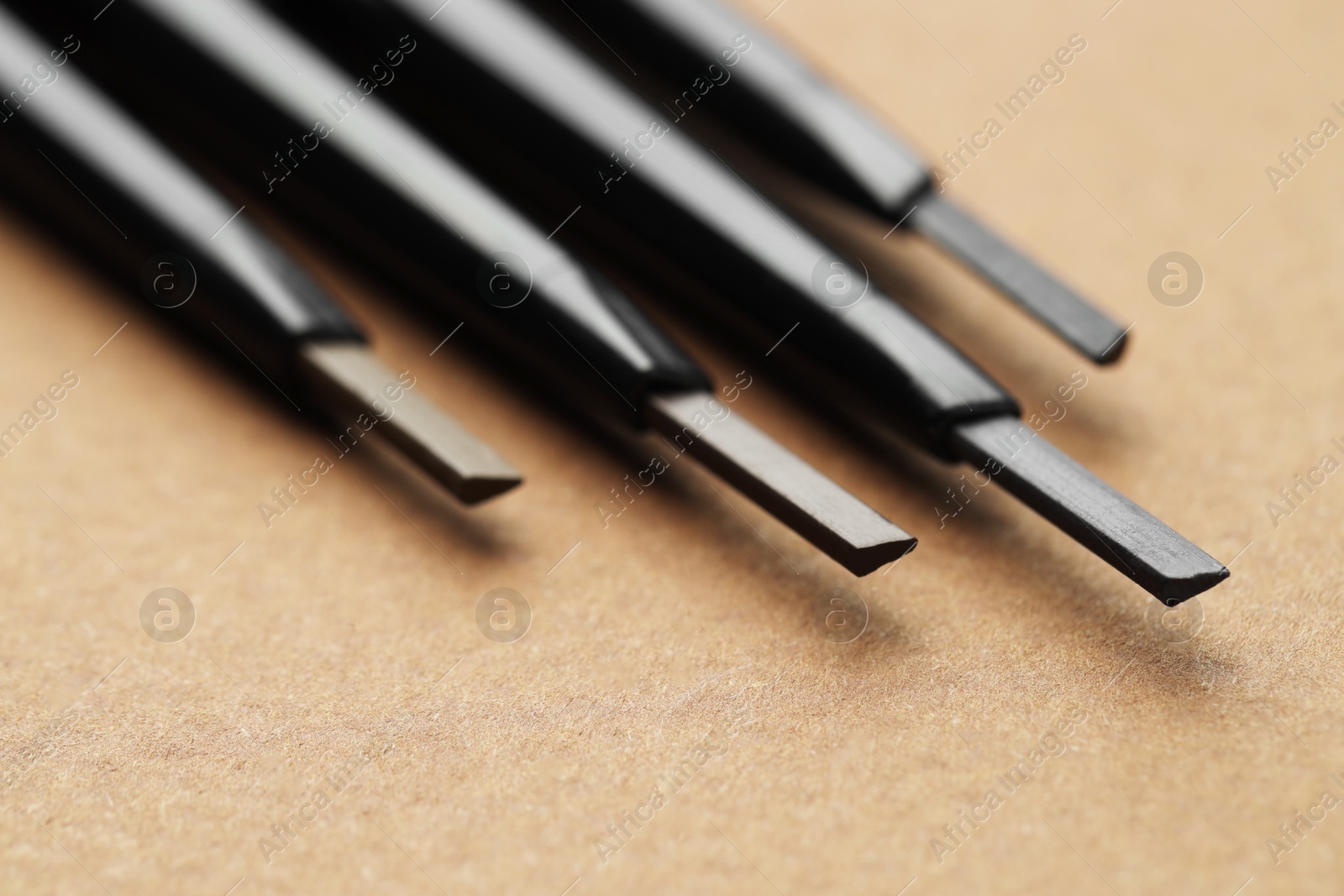 Photo of Automatic eyebrow pencils on brown background, macro view