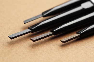 Photo of Automatic eyebrow pencils on brown background, macro view