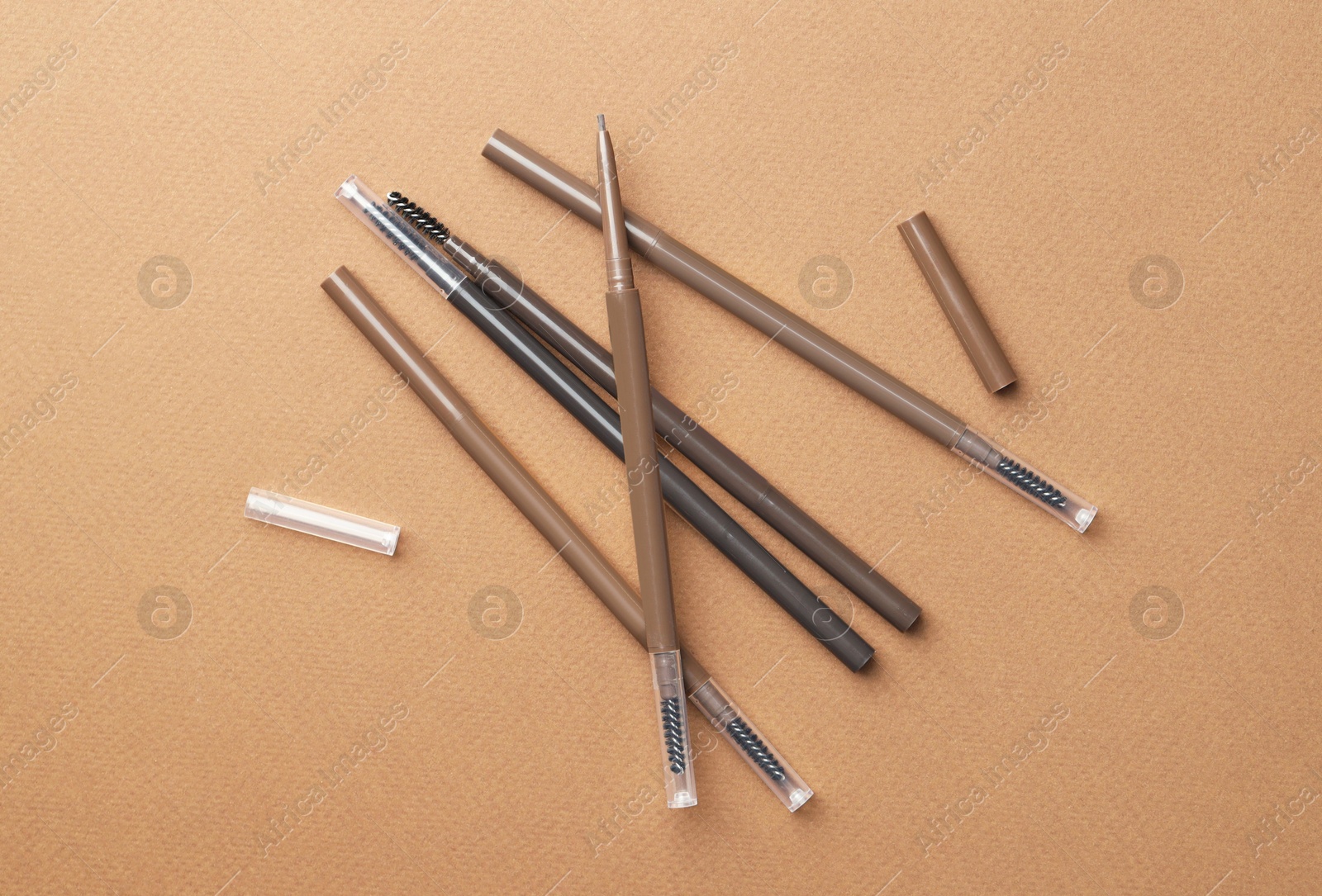 Different eyebrow pencils on brown background, flat lay Photo of Different eyebrow pencils on brown background, flat lay