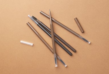 Photo of Different eyebrow pencils on brown background, flat lay