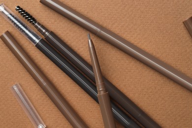Photo of Different eyebrow pencils on brown background, flat lay