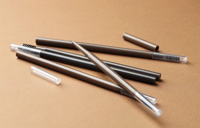 Photo of Automatic eyebrow pencils on brown background, closeup