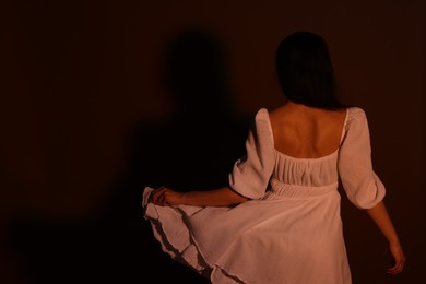 Photo of Woman in dress on dark brown background, back view. Space for text