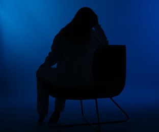 Photo of Silhouette of woman on chair against dark blue background