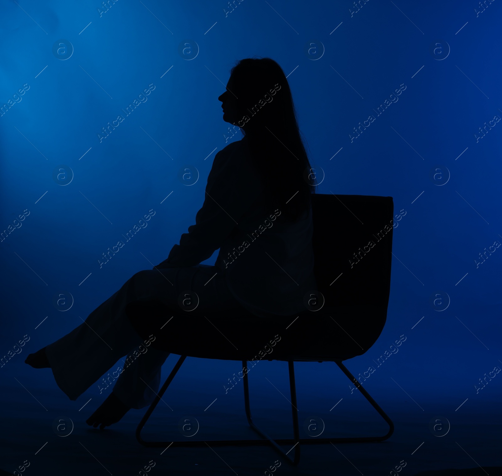 Photo of Silhouette of woman on chair against dark blue background