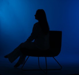 Photo of Silhouette of woman on chair against dark blue background