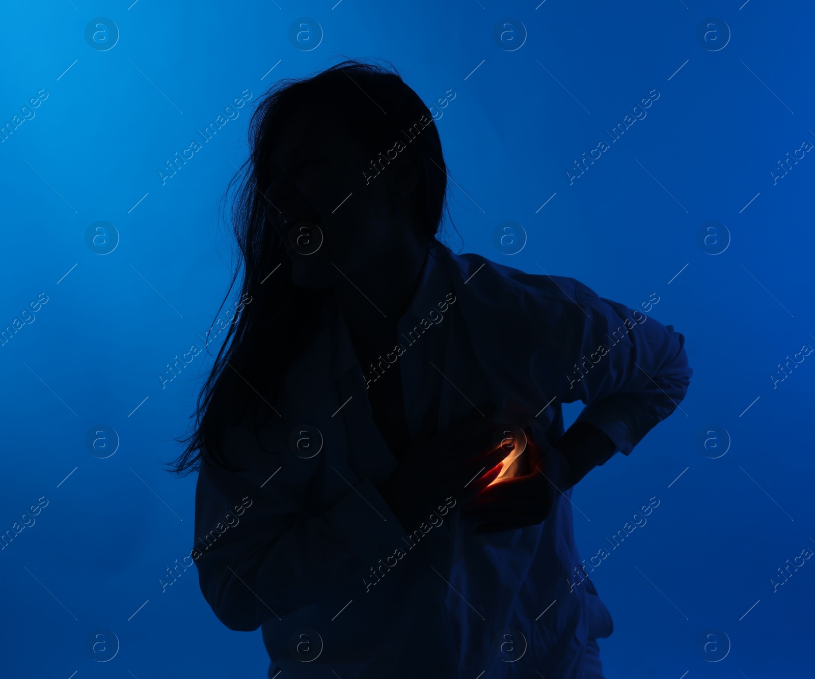 Silhouette of woman with light near her chest dark blue background Photo of Silhouette of woman with light near her chest dark blue background