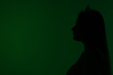 Photo of Silhouette of woman with crown on dark green background, space for text
