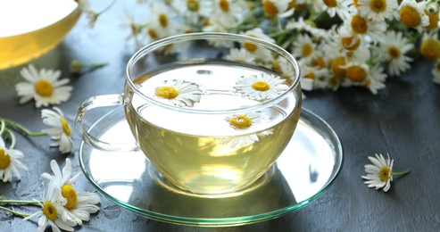 Photo of Tasty chamomile tea and flowers on grey table, closeup