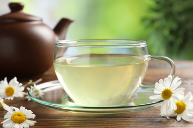 Photo of Tasty chamomile tea and flowers on wooden table, closeup