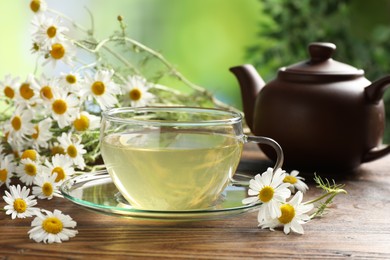 Photo of Tasty chamomile tea and flowers on wooden table, closeup