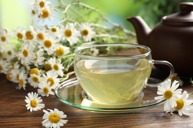 Photo of Tasty chamomile tea and flowers on wooden table, closeup