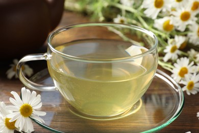 Photo of Tasty chamomile tea and flowers on wooden table, closeup
