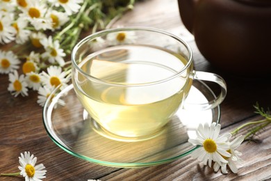 Photo of Tasty chamomile tea and flowers on wooden table, closeup