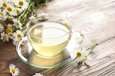 Photo of Tasty chamomile tea and flowers on wooden table, closeup. Space for text