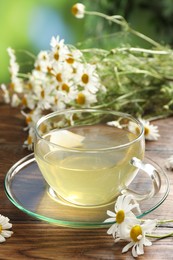 Photo of Tasty chamomile tea and flowers on wooden table, closeup