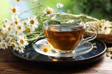 Photo of Tasty chamomile tea and flowers on wooden table, closeup