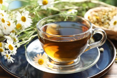 Photo of Tasty chamomile tea and flowers on wooden table, closeup