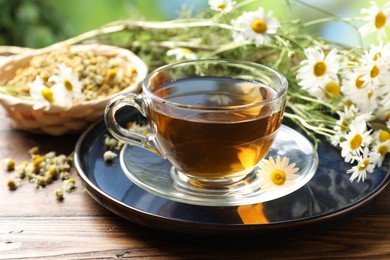 Photo of Tasty chamomile tea and flowers on wooden table, closeup