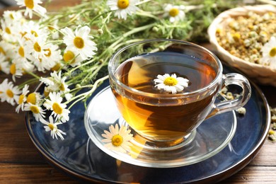 Photo of Tasty chamomile tea and flowers on wooden table, closeup