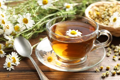 Photo of Tasty chamomile tea and flowers on wooden table, closeup