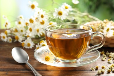 Photo of Tasty chamomile tea and flowers on wooden table, closeup
