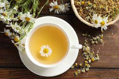 Photo of Tasty chamomile tea and flowers on wooden table, flat lay