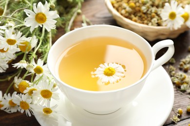 Photo of Tasty chamomile tea and flowers on wooden table, closeup