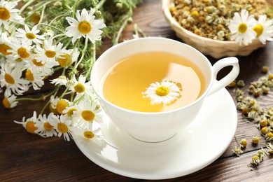 Photo of Tasty chamomile tea and flowers on wooden table, closeup
