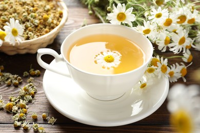 Photo of Tasty chamomile tea and flowers on wooden table, closeup