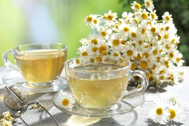 Photo of Tasty chamomile tea, infuser and flowers on light grey table, closeup
