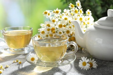 Photo of Tasty chamomile tea and flowers on light grey table, closeup
