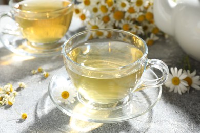 Photo of Tasty chamomile tea and flowers on light grey table, closeup