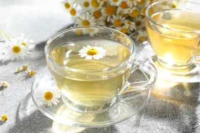 Photo of Tasty chamomile tea and flowers on light grey table, closeup