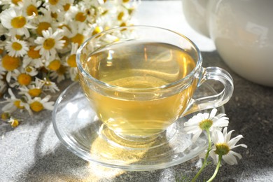 Photo of Tasty chamomile tea and flowers on light grey table, closeup