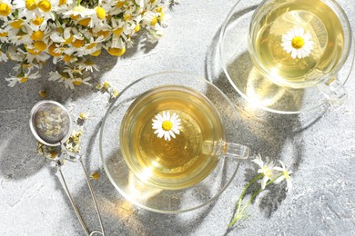 Photo of Tasty chamomile tea, infuser and flowers on light grey table, flat lay