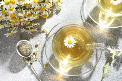 Photo of Tasty chamomile tea, infuser and flowers on light grey table, flat lay