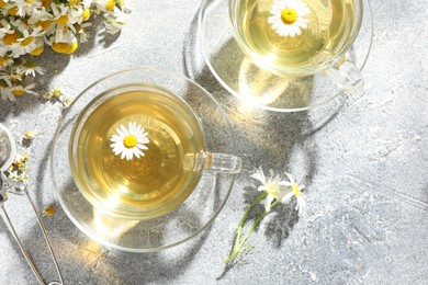 Photo of Tasty chamomile tea, infuser and flowers on light grey table, flat lay