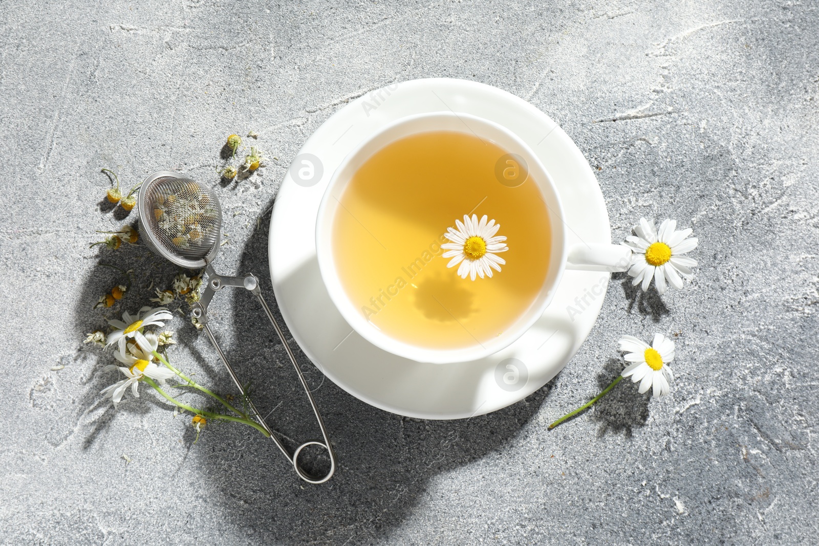 Photo of Tasty chamomile tea, infuser and flowers on light grey table, flat lay